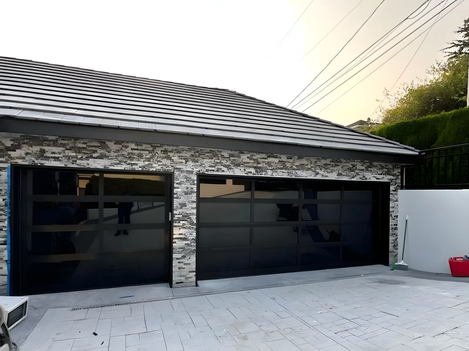 Two black full-view glass garage doors on a stone-veneer garage