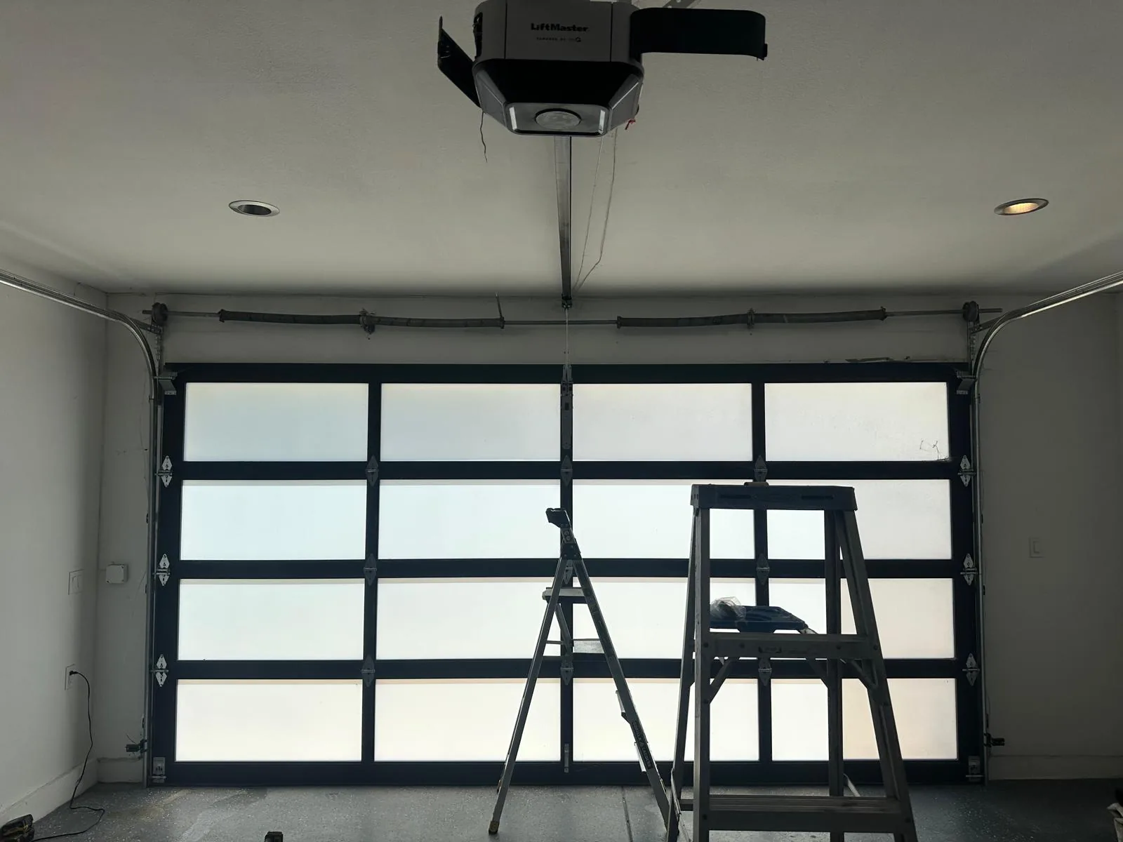 Inside a garage with a full-view frosted glass door, the opener overhead and two ladders